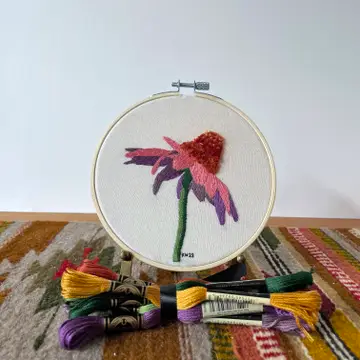 A finished version of the Coneflower embroidery kit sitting on a table along with some skeins of embroidery floss. 