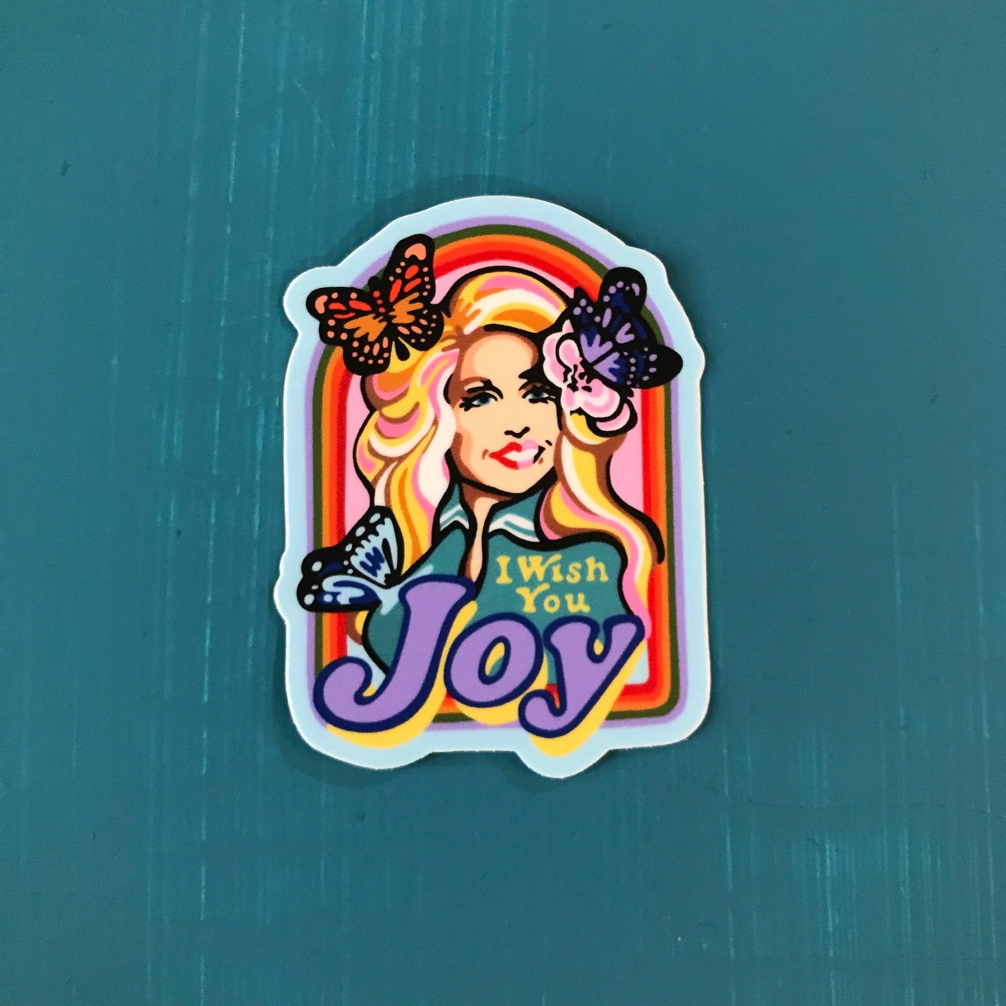 Vinyl sticker with an illustration of Dolly Parton. It says "I wish you joy" and she has butterflies in her hair. 