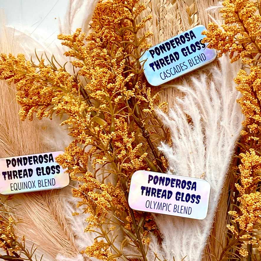 Several tins of Ponderosa Thread Gloss scattered onto a background of dried florals. 