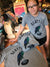 A stack of folded t-shirts that say Seattle and have a hawk carrying a football depicted on them. A young girl is modeling the xs size shirt.
