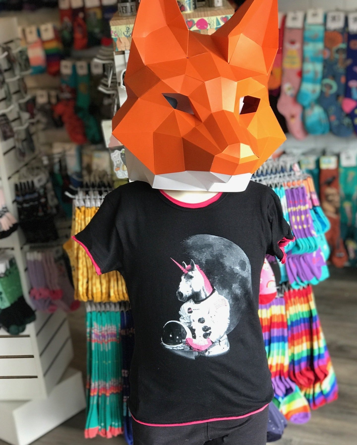 A paper fox head on top of a youth mannequin. The mannequin is wearing a black youth tshirt with a unicorn astronaut on the front. 
