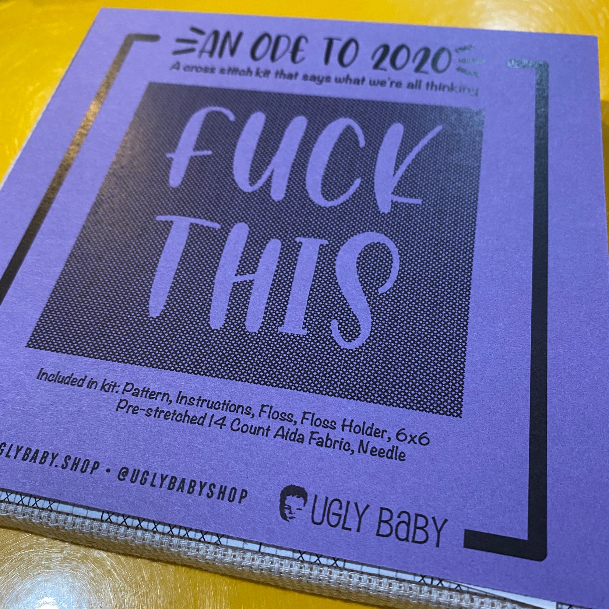 A cross stitch kit. The packaging is purple and says "An ode to 2020. Fuck this." The packaging is dark purple against a bright yellow background.