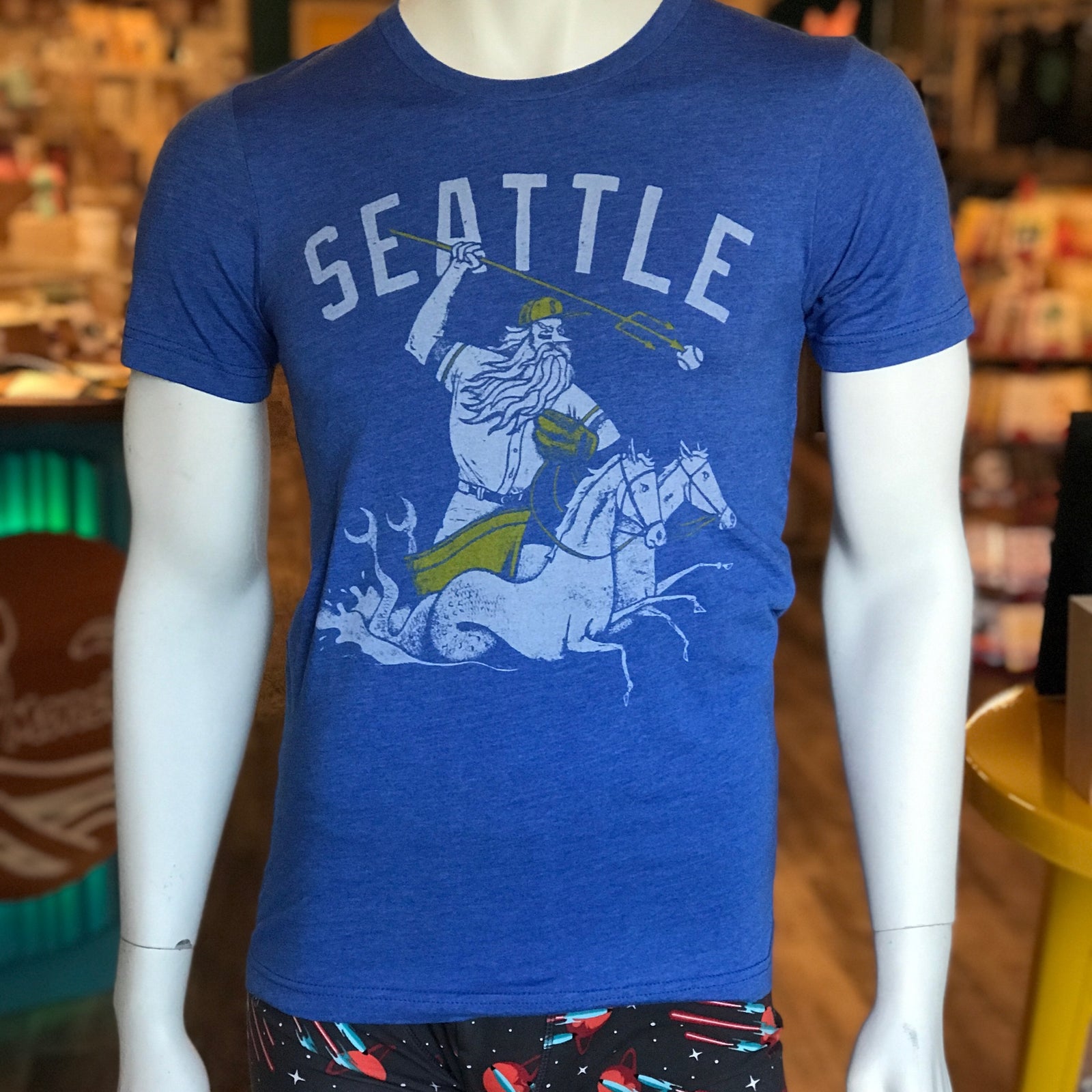 Blue unisex crew t-shirt by Factory 43. It says Seattle and has a mariner wearing a baseball hat and glove and being pulled by two horse mermaids. 