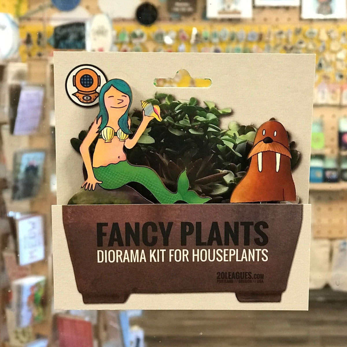 Close up photo of a Fancy Plants Diorama Kit for Houseplants by 20 Leagues. This one has a mermaid with blue hair wearing a shell bra. She is holding a shell &amp; sitting next to a walrus with long tusks. 