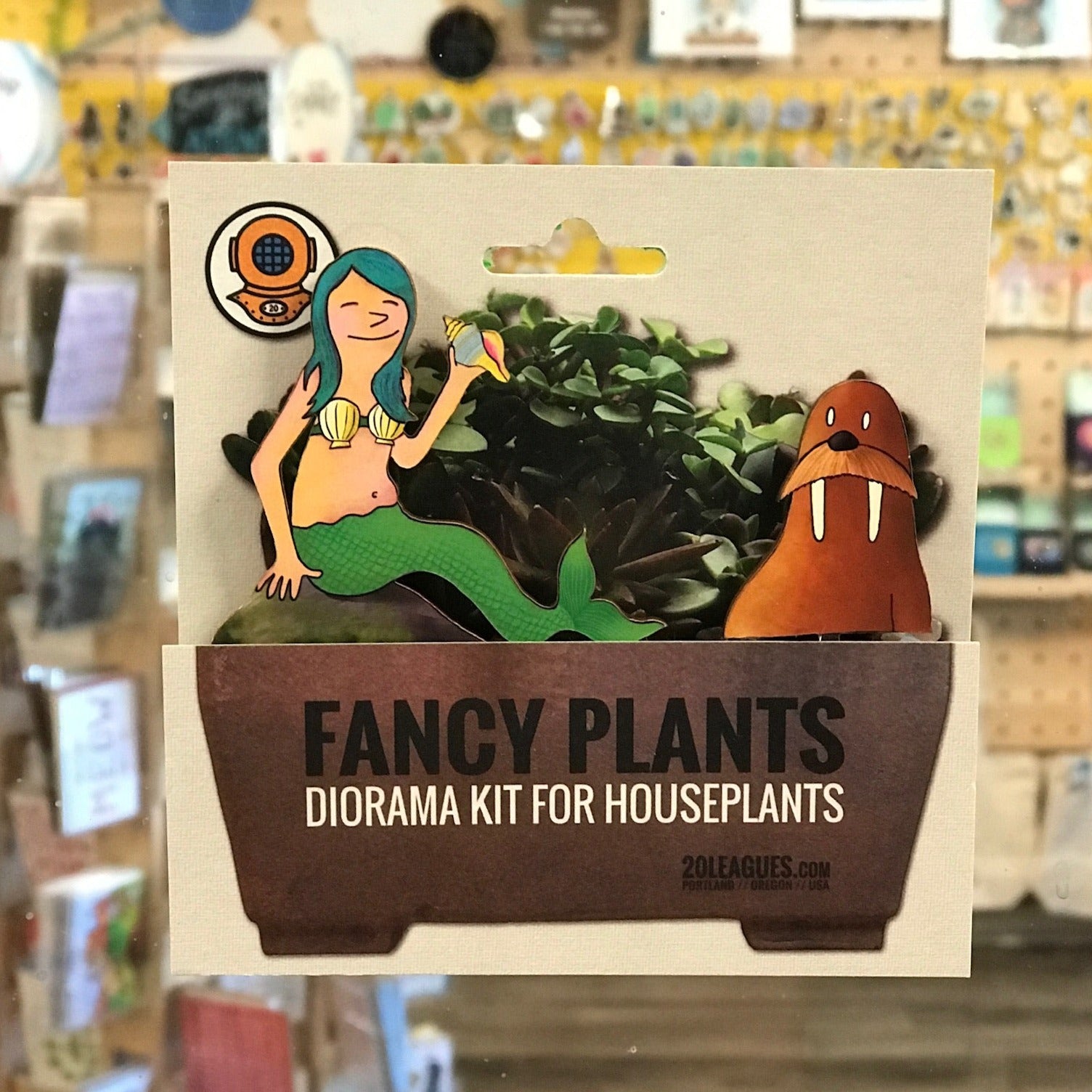 Close up photo of a Fancy Plants Diorama Kit for Houseplants by 20 Leagues. This one has a mermaid with blue hair wearing a shell bra. She is holding a shell & sitting next to a walrus with long tusks. 