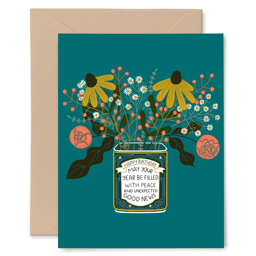 A greeting card sits atop a tan colored envelope. The card is dusty green and has a bouquet of flowers in a vase. The vase says, "Happy Birthday. May your year be filled with peace and unexpected good news."