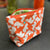 Example of a lined zipper pouch with a box bottom so it stands on its own. The exterior fabric is orange and white and the interior is lime green and white. It has a bright orange zipper.