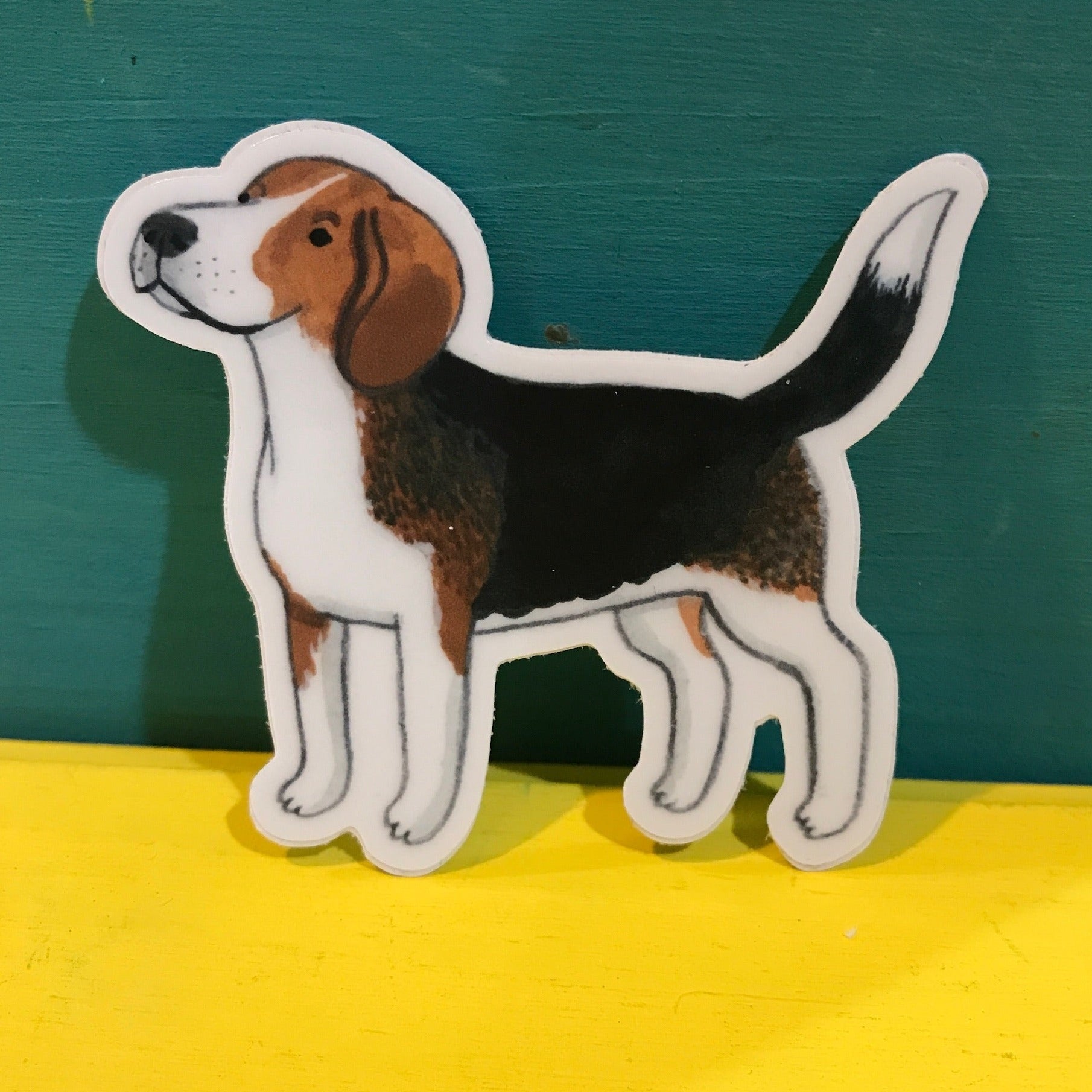 Watercolor illustration of a Beagle dog in sticker form. It's standing up against a yellow and teal background.