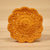 A round crocheted coaster with a scalloped edge. It is light orange and set against a woodgrain background. 