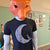 A dark heather gray t-shirt by Factory 43. It is shown on a mannequin with a fox head made out of orange paper. The shirt has a crescent moon screenprinted in white. On the curve of the moon, there is a wolf wearing an astronaut suit. The wolf is howling. 